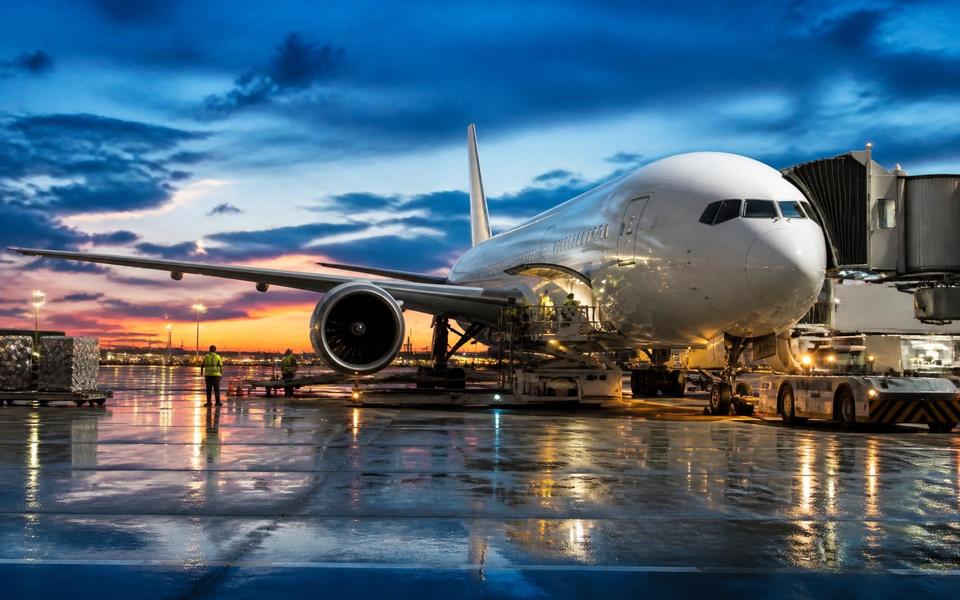 A widebody aircraft at the gate on a wet apron at dusk